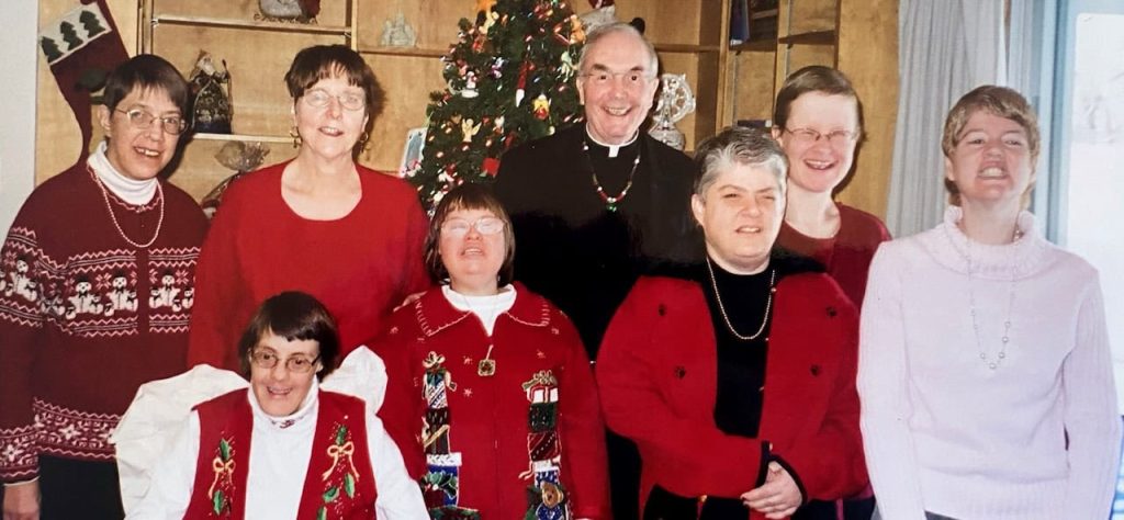 A Christmas photo of a group of people in festive sweaters. There is a Christmas tree behind them.