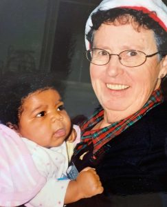 A woman in a Santa hat smiles as she is holding a baby.