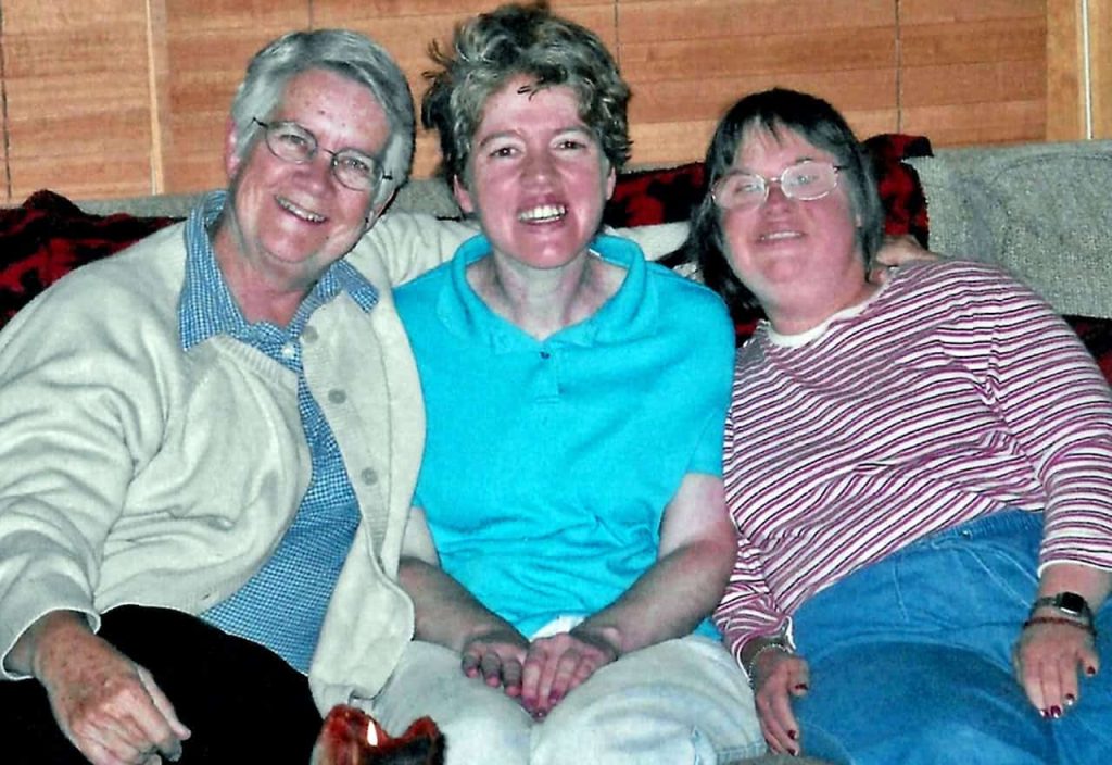 An older nun with grey hair is smiling with her arm over two residents of the community where they live.