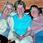 An older nun with grey hair is smiling with her arm over two residents of the community where they live.