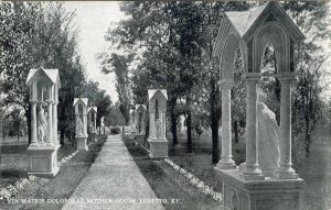A black-and-white postcard looking down the walk leading into the Loretto Motherhouse Cemetery with the stations of the Seven Dolors along the way. Text at the bottom of the postcard reads "Via Matris Dolorosae Mother House. Loretto. KY."