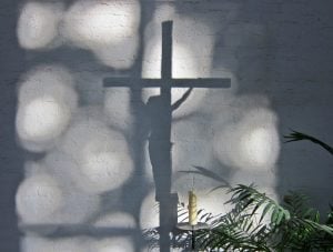 Shadow of a crucifix on a white-painted brick wall.