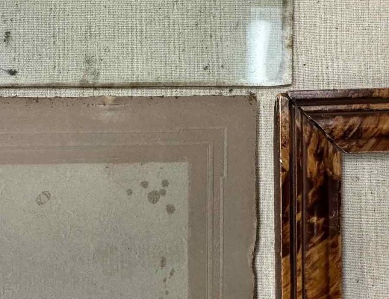 The corners of a frame, old stained matboard and spotted frame glass come together in this photo.