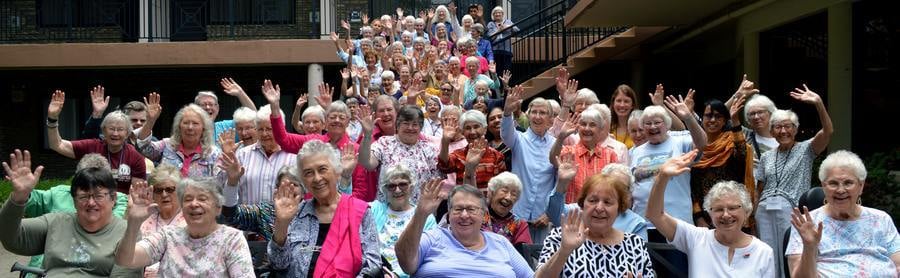 A large group of over 50 people waving and smiling to the camera.