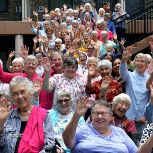 A large group of over 50 people waving and smiling to the camera.