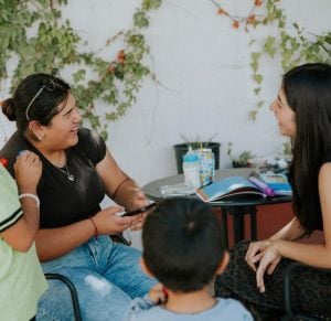 Two Latina women smiling and laughing as they sit at a table together.