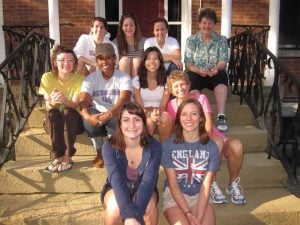 A group of eight women volunteers and two middle aged women sitting staggered on steps smiling for a group photo.