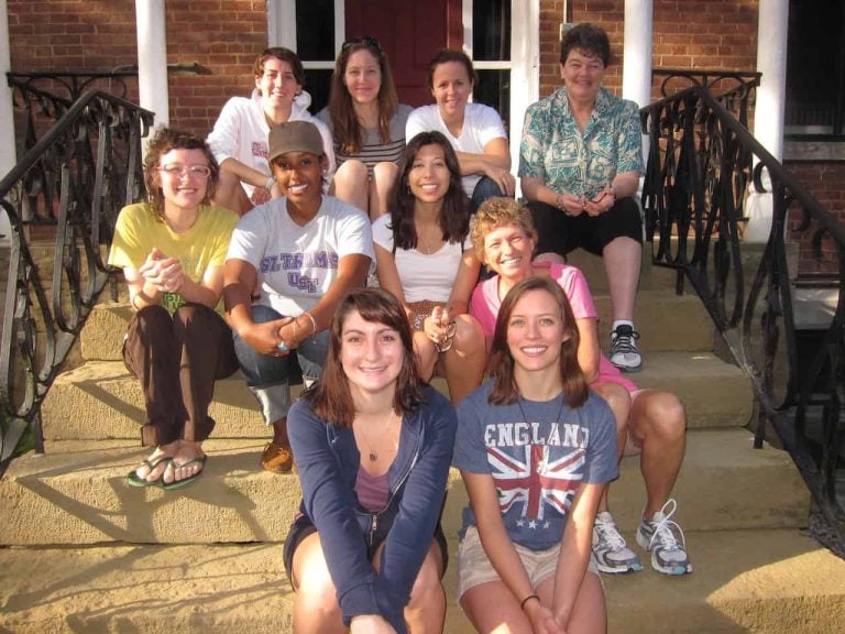 A group of eight women volunteers and two middle aged women sitting staggered on steps smiling for a group photo.