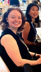 Two young college students smiling for a photo sitting next to each other at a restaurant.