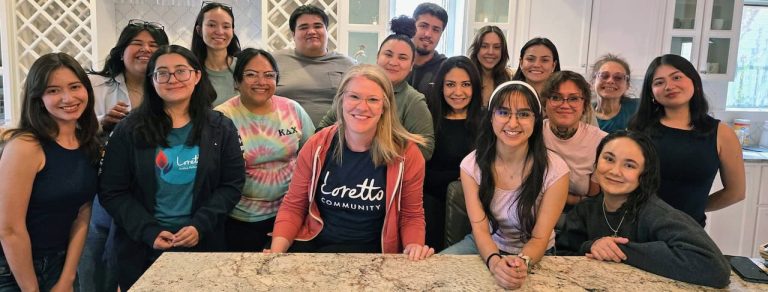 A large group 16 Latino college students of varying ages and one white woman in her 40s smiling together at an end of year retreat.