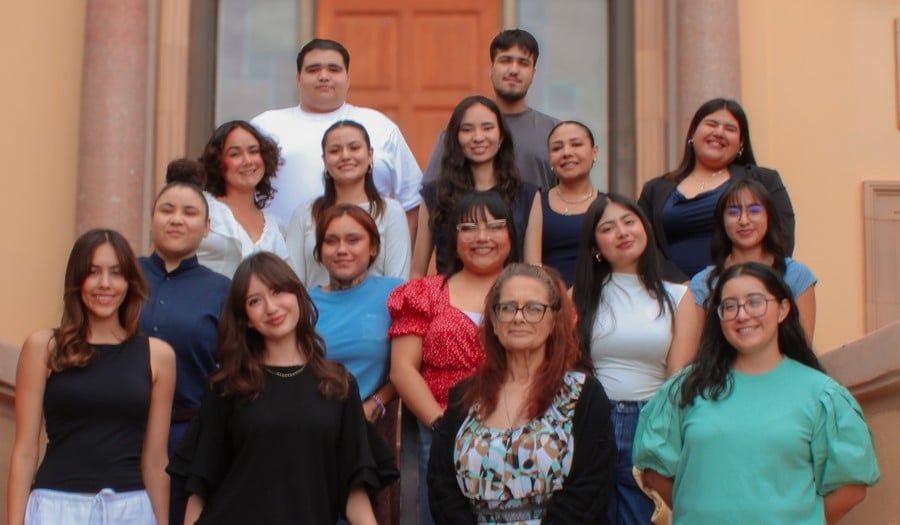 A group photo of 16 people of different ages, genders and backgrounds taken on the front steps of a building.