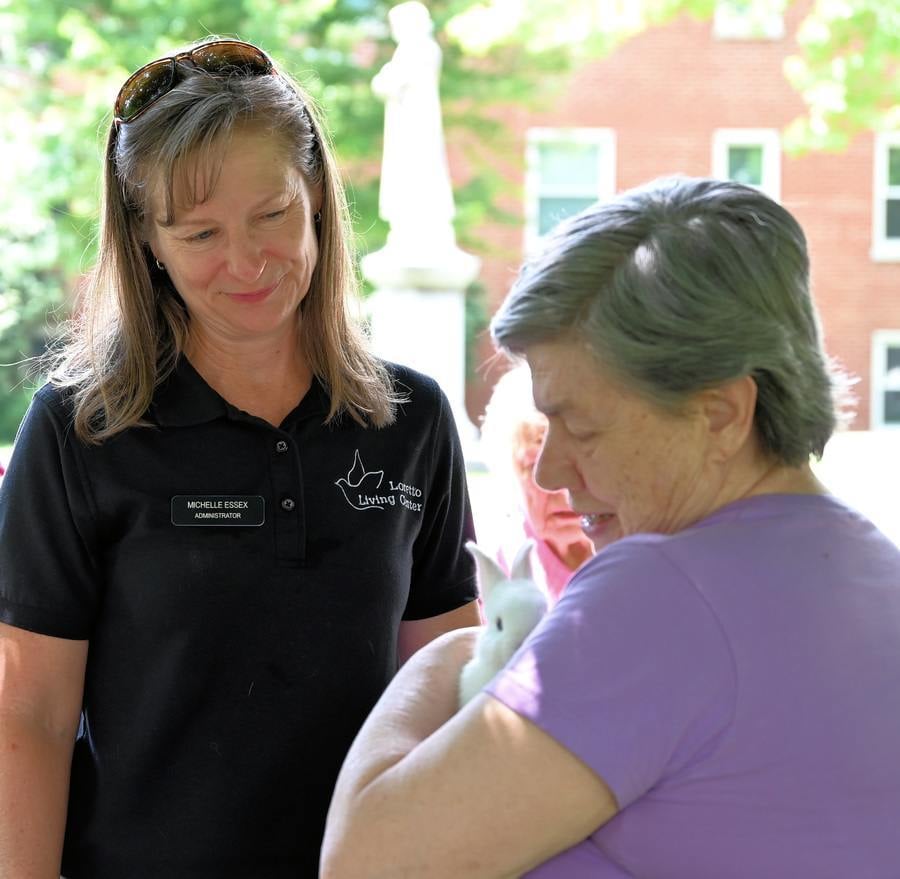 Loretto Living Center administrator Michelle Essex looks on as retired Sister Denise Ann Clifford SL holds a white rabbit outside the Motherhouse builidings.