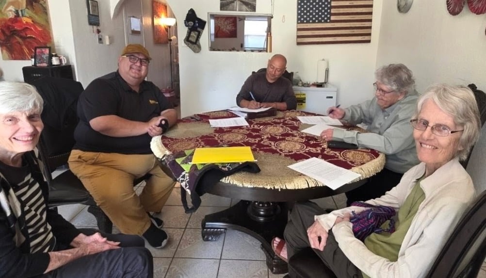 Three women and two men are sitting at a round table signing a lease.