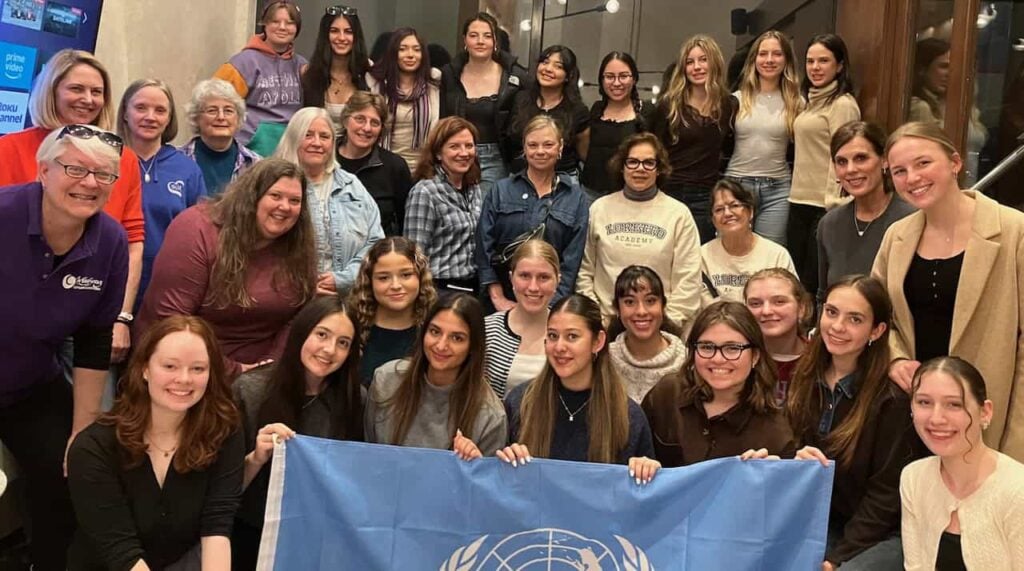 A group of about 30 people, high school students, teachers, and U.N. staff standing together for a group photo holding the United Nations blue flag at the Commission on the Status of Women 2026.