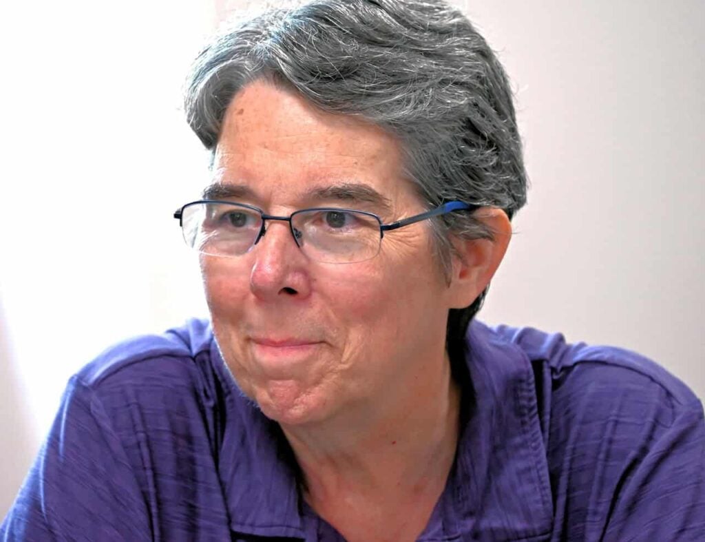 An older woman with grey hair glasses and a purple shirt listens intently.