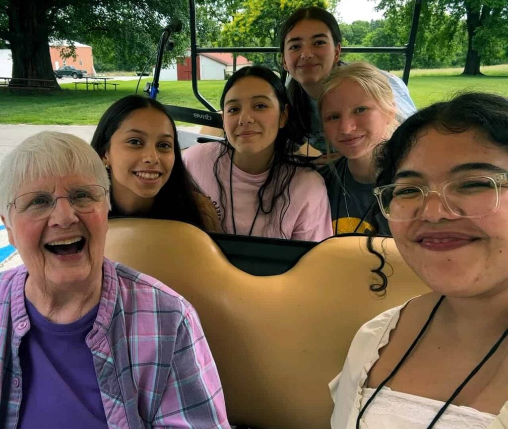 A group of five high school girls smile with a nun on a golf cart outside.