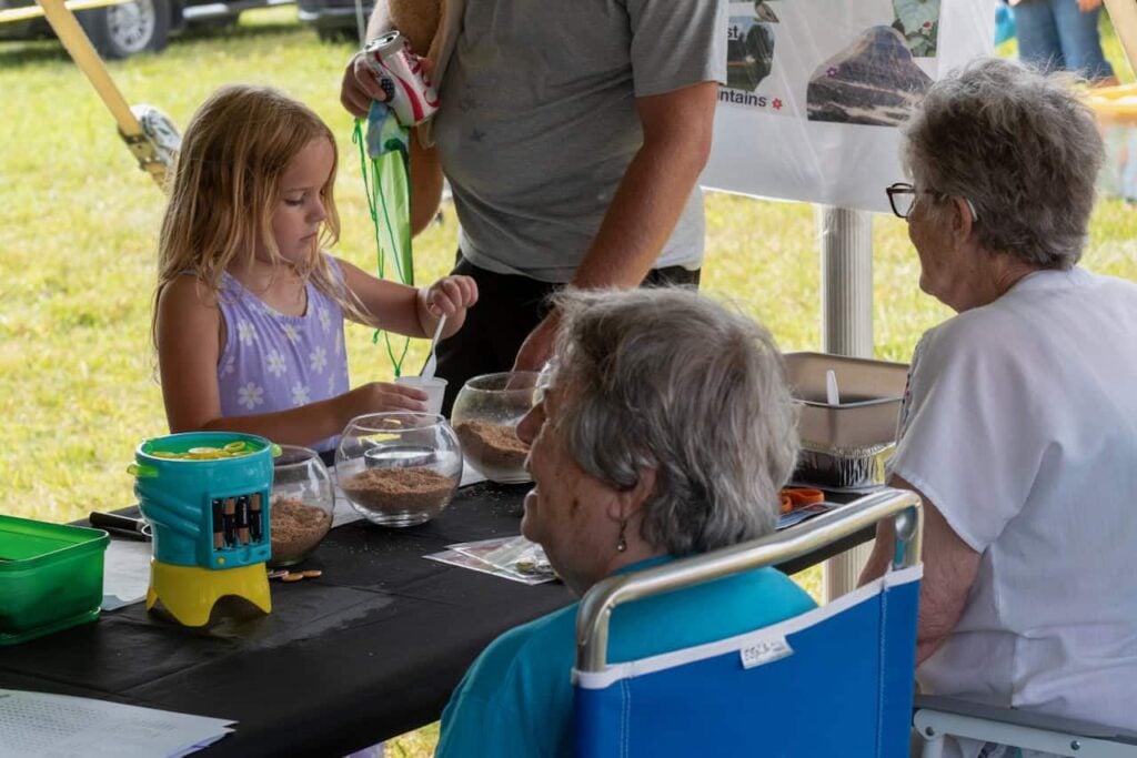 A little girl is shown putting soil into a cup at an event table outside at Ag Bash 2026