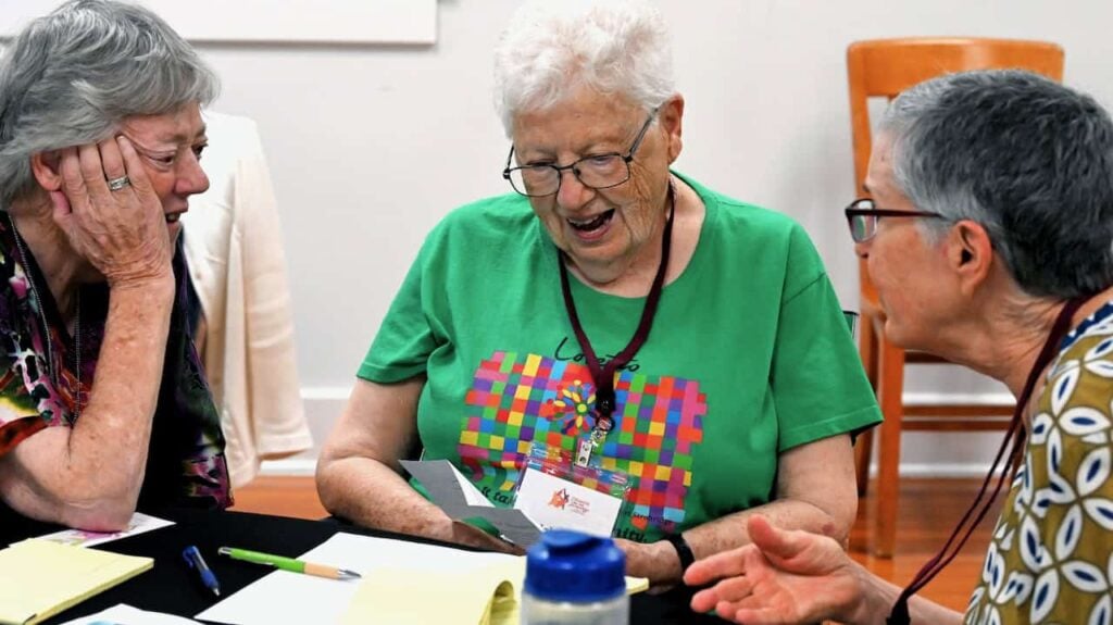 Three older women sitting at a table during a gathering having a lively discussion with one another.