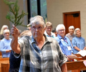 An older woman with gray hair sprinkles holy water in a church