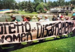 People carry a large banner reading "Loretto Women for Disarmament" in a protest march on the grass.