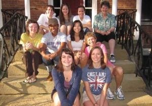 A group of eight women volunteers and two middle aged women sitting staggered on steps smiling for a group photo.