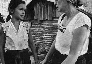 A woman holds a young girl's hand and talks with her.