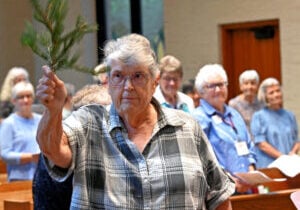 An older woman with gray hair sprinkles holy water in a church