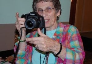 A woman smiles from behind her camera.