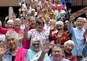 A large group of over 50 people waving and smiling to the camera.