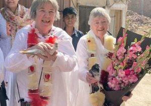 Two women in traditional Pakistani tunics hold pigeons and a huge bouquet of gladiolas.