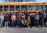 A group of young volunteers smiling together in front of a school bus.