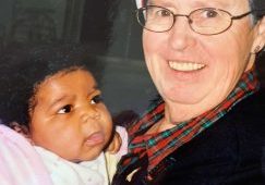 A woman in a Santa hat smiles as she is holding a baby.