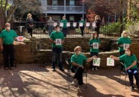 People wearing green shirts and N95 masks pose in a multilevel courtyard, holding letters that together read "WE ARE BLESSED."
