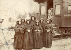 Archival photo of seven nuns in habits standing in front of a train car.