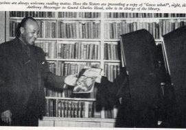 Archival news clipping of a photo of two nuns in habits handing a magazine to a Black man in a suit standing in front of a wall of bookshelves. The caption across the top reads "Magazines are always welcome reading matter. Here the Sisters are presenting a copy of 'Guess what?', right, the St. Anthony Messenger to Guard Charles Head, who is in charge of the library.