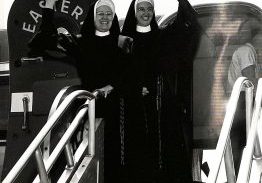 Archival photo of two sisters in habit waving from the door of a plane.