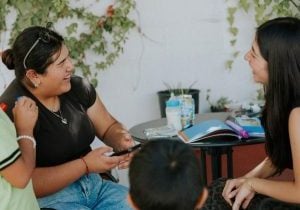 Two Latina women smiling and laughing as they sit at a table together.