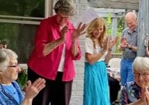 Two women turning 90 are shown smiling and being celebrated by people all around them at a party clapping and smiling