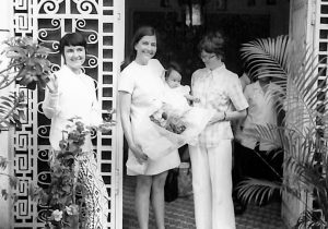 Three women, one holding a baby stand in a doorway in this black and white archival photo.