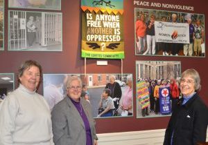 Three women smile in front of a wall of historical photos