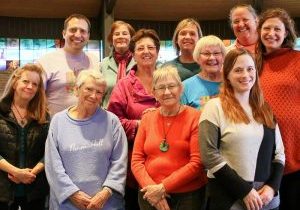 A smiling group of people, ranging in age from young adults to seniors, pose for a group photo.