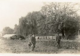 Black and white archival photo of two men standing by a large garden.