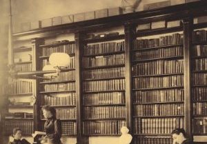 An old sepia toned photo of students studying in a library in front tall bookshelves.