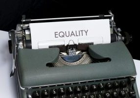 A closeup of an old typewriter with the word "equality" in large print on the paper coming out of the top.